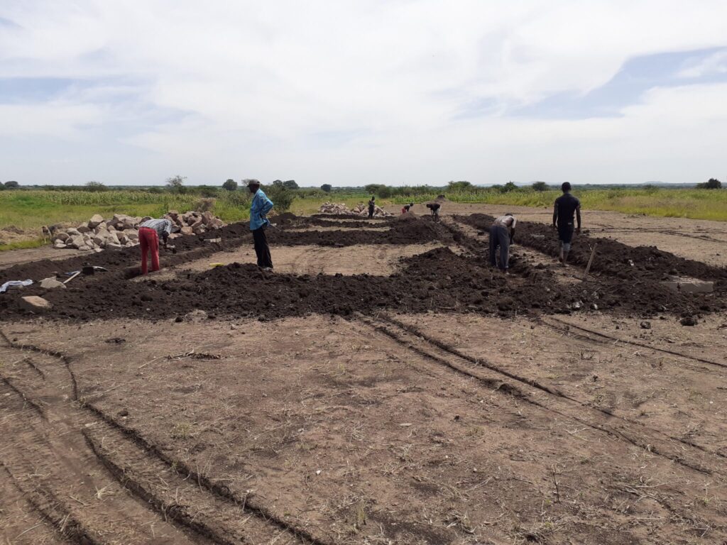 Group of people working in a field with piles of rocks nearby.