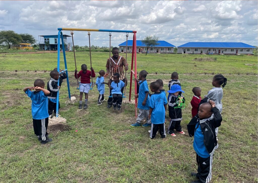 A group of young children playing outside on a swing set with a teacher supervising.