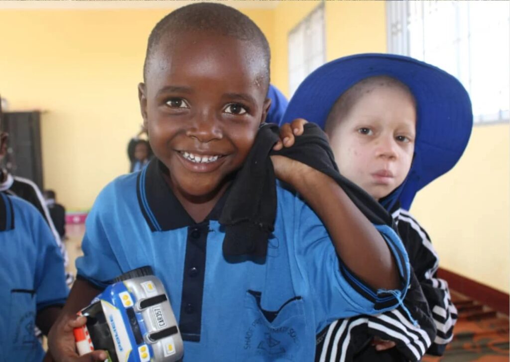 Two young children in blue uniforms, one smiling at the camera, the other wearing a blue sunhat.