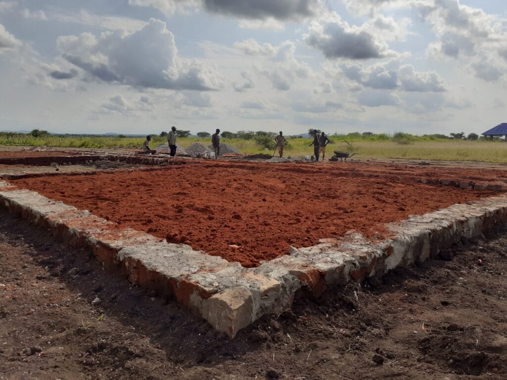 Workers preparing a foundation filled with red soil.