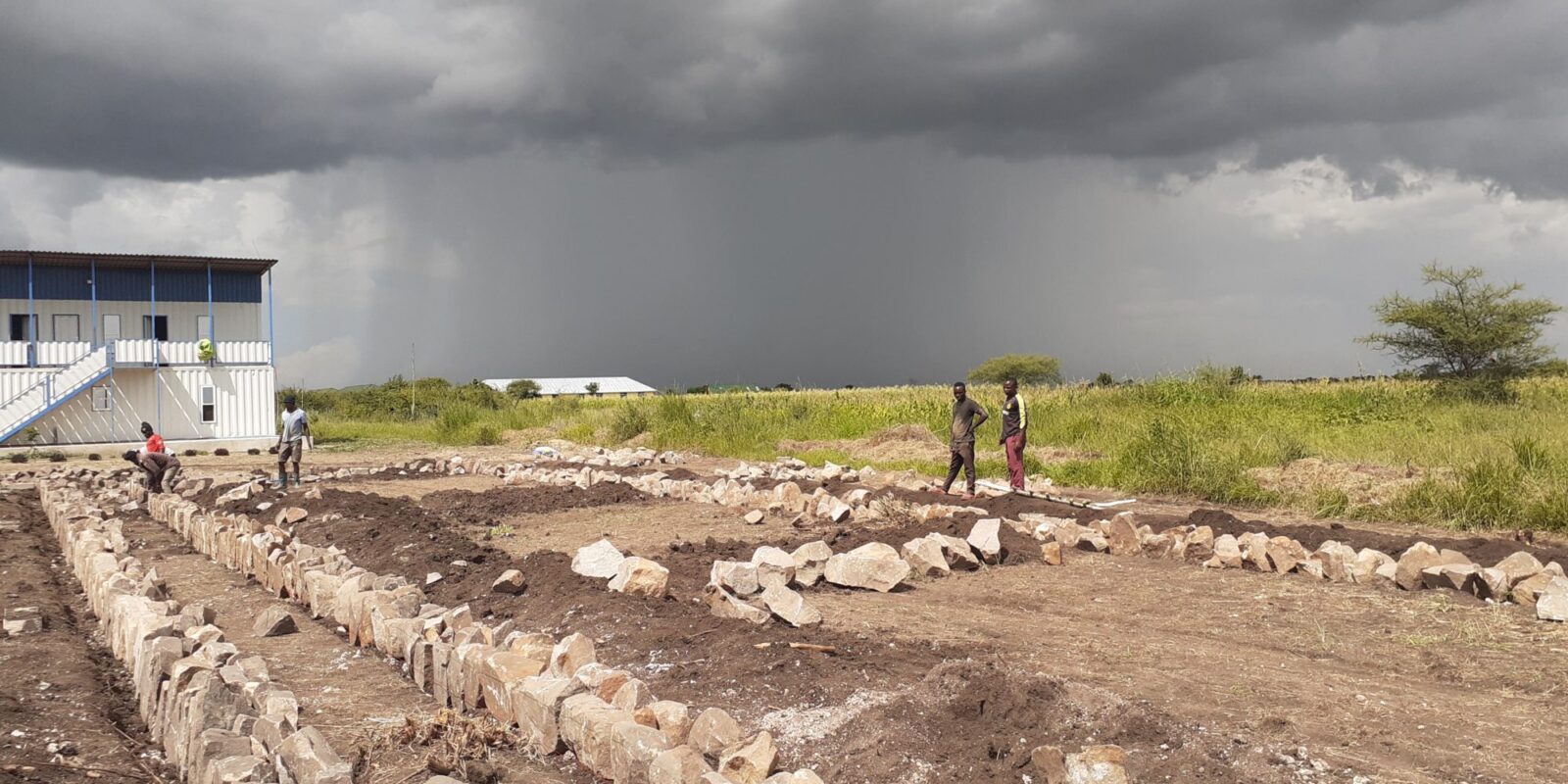 Construction site with workers under dark stormy skies.