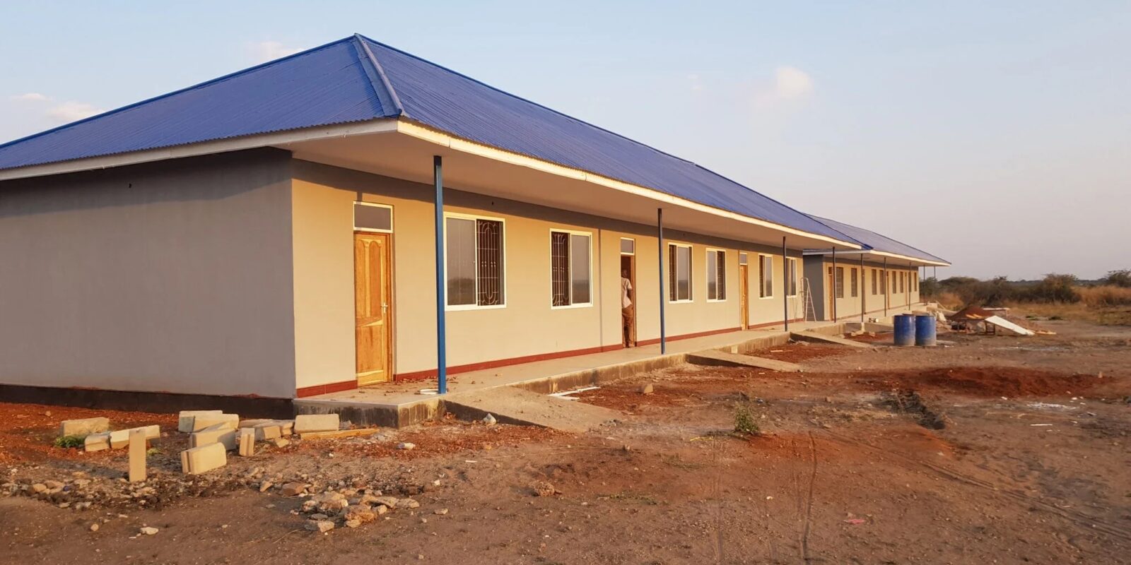 Long building with a blue roof and multiple doors.