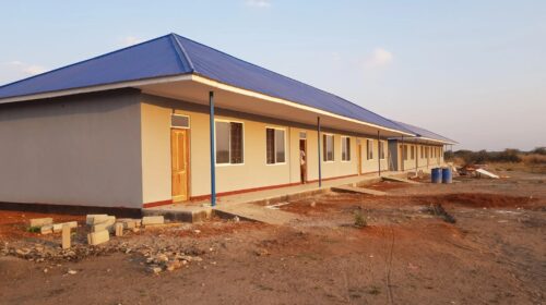 Long building with a blue roof and multiple doors.