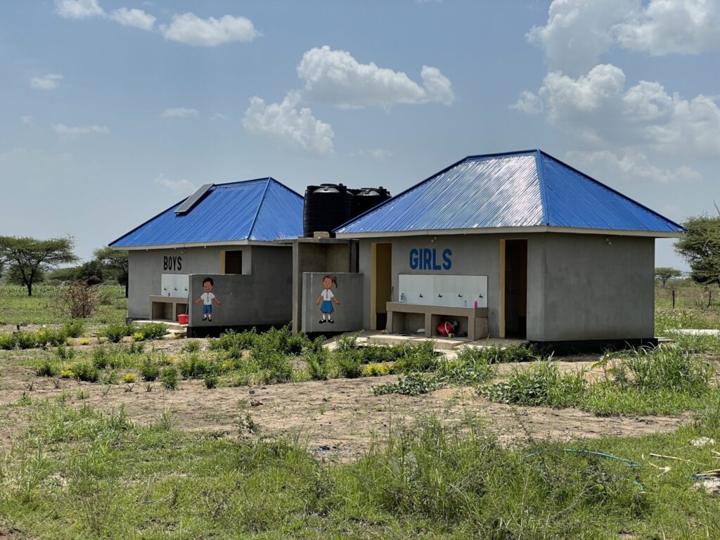 Restroom buildings for boys and girls with blue roofs in a rural area.