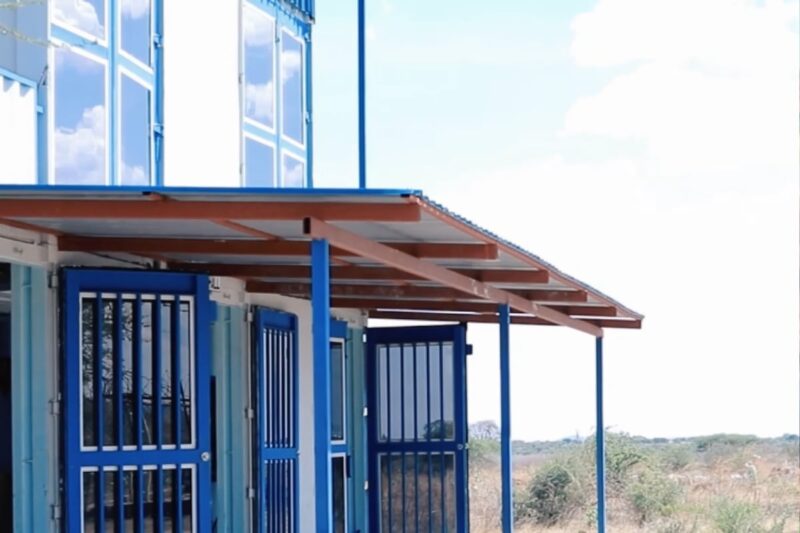 Shows a building labeled “Clinic” with blue doors and a shaded veranda. This suggests a medical facility available for healthcare services within the community.