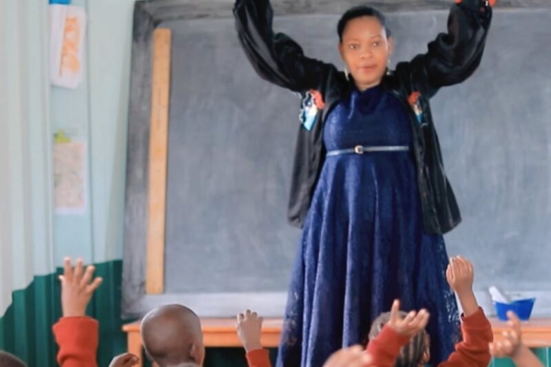 Shows a teacher engaging with young children in a classroom, signifying the educational facilities available for children in the community.