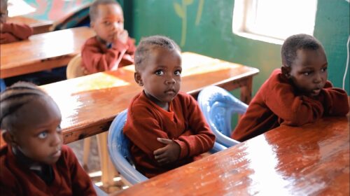 Children sitting at wooden desks in a classroom.